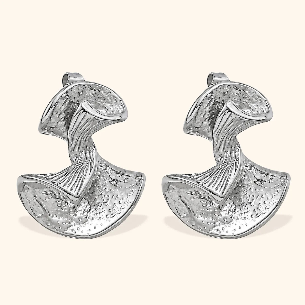 A pair of textured silver earrings with a sculptural, organic shape, displayed on a light cream background.